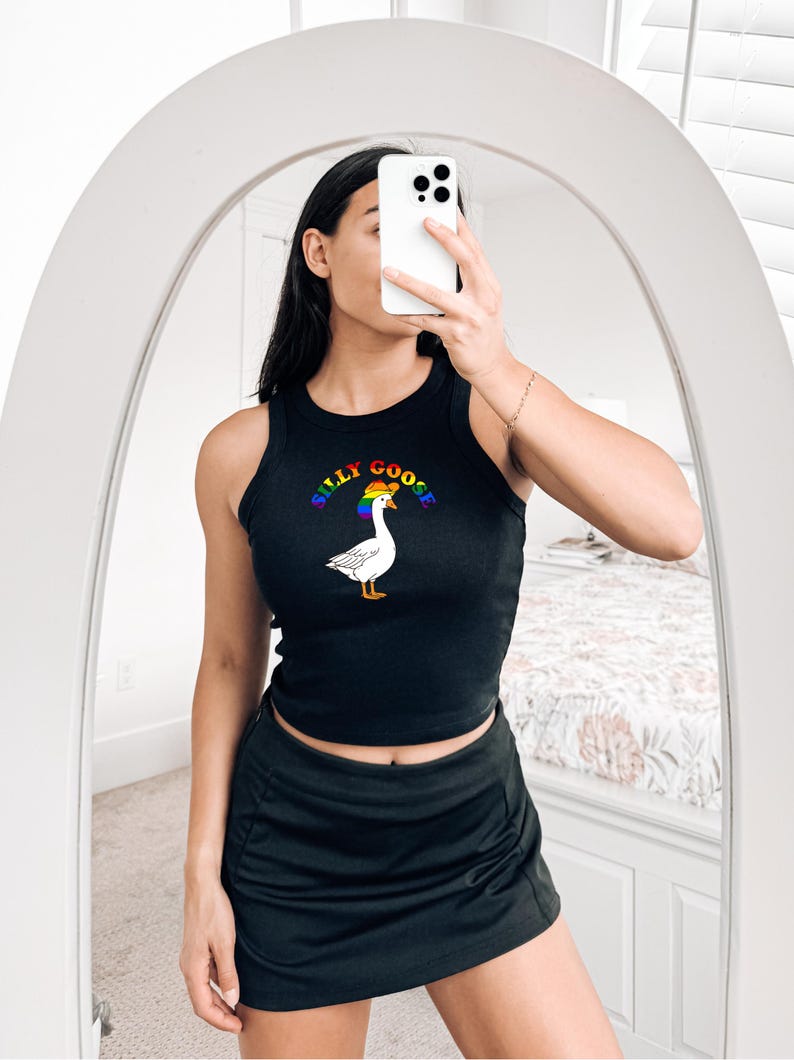 Op de afbeelding: Zwarte tanktop met de tekst "Silly Goose" boven een witte gans met een regenbooghoed. De tanktop wordt gecombineerd met een zwarte rok. De foto is genomen voor een spiegel.