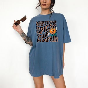 May include: A blue t-shirt with the text "WHATEVER SPICES YOUR PUMPKIN" in black and orange. The graphic includes a smiling pumpkin with green leaves. The shirt is short-sleeved and has a relaxed fit.