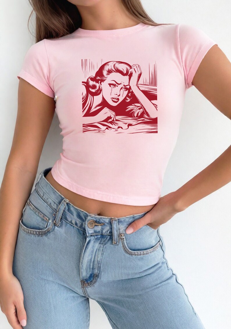 Pu&ograve; includere: Una maglietta rosa corta con una stampa grafica rossa di una donna che piange. La donna &egrave; disegnata in stile fumetto.