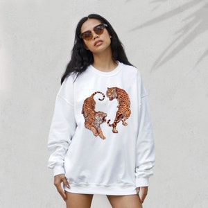 May include: White sweatshirt with a graphic print of two tigers facing each other. The tigers are orange and black with white stripes.