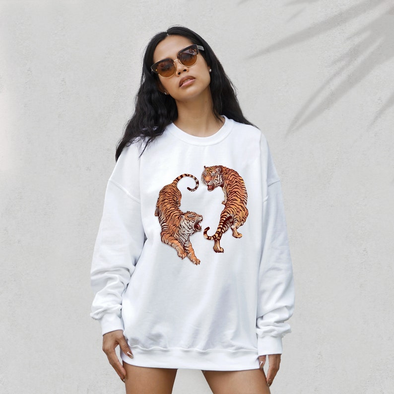 May include: White sweatshirt with a graphic print of two tigers facing each other. The tigers are orange and black with white stripes.