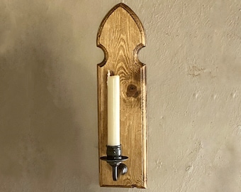 Könnte beinhalten: Ein Wand-Kerzenhalter aus Holz mit einer spitzen Oberseite und einem einzelnen Kerzenhalter. Der Kerzenhalter ist aus Naturholz mit rustikalem Finish. Der Kerzenhalter ist leer und bereit für den Gebrauch.