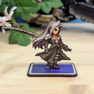 Könnte beinhalten: Pixelige Figur eines Charakters mit langen silbernen Haaren und einem schwarzen Mantel, der ein langes Schwert hält. Die Figur steht auf einer blauen rechteckigen Basis mit schwarzem Rand. Der Hintergrund umfasst Grün und ein dunkles Objekt.