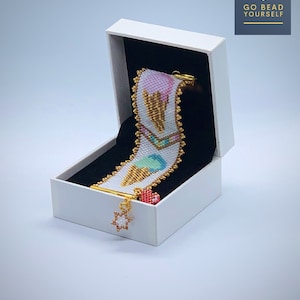 Peut inclure: Un bracelet blanc perlé avec un motif de crème glacée coloré et des accents dorés. Le bracelet est dans une boîte blanche avec un intérieur noir. La boîte a un petit charme doré attaché à elle.