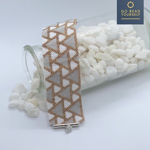 May include: A white, gray, and gold beaded bracelet with a geometric pattern of triangles. The bracelet is lying on a white surface and has a silver clasp.