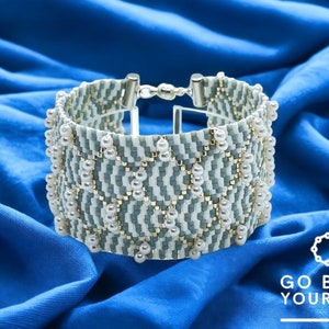 May include: A white and gray beaded bracelet with a geometric pattern and white pearl accents. The bracelet is on a blue fabric background. The text "GO BEAD YOURSELF" is visible in the lower right corner of the image.