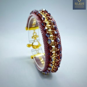 Puede incluir: Un brazalete de cuentas rosa y dorado con un cierre transparente. El brazalete está hecho con pequeñas cuentas facetadas en tonos rosa, dorado y morado.
