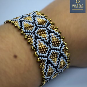 以下が含まれることがあります： 金、黒、白のビーズを使った幾何学模様の幅広ビーズブレスレット。ブレスレットは手首に着用されています。縁は金のビーズでトリミングされています。「GO BEAD YOURSELF」という文字が右上隅にあります。