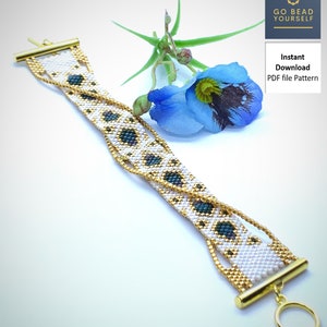 May include: A white and gold beaded bracelet with a green and blue geometric pattern. The bracelet has a toggle clasp and is shown on a white background with a blue flower.