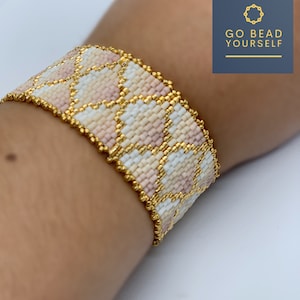 Op de afbeelding: Een kralenarmband met een geometrisch patroon in roze, wit en gouden tinten. De armband is gemaakt van kleine kralen en heeft een gouden rand.