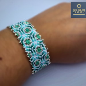 May include: A white and green beaded bracelet with a geometric pattern. The bracelet is made with small, round beads and has a silver trim. The bracelet is on a person's wrist.