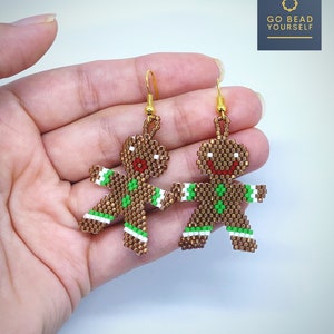 May include: A pair of gingerbread man earrings made with brown, white, green, and red beads. The earrings are hanging from gold hooks.