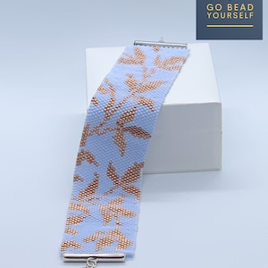 Puede incluir: Un brazalete de cuentas azul claro con un patrón de hojas doradas. El brazalete tiene un cierre plateado.