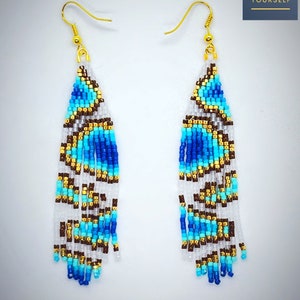 May include: A pair of long, beaded earrings with a geometric pattern in shades of blue, white, brown, and gold. The earrings are made with small seed beads and have a dangling design.