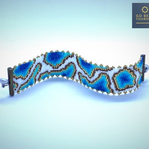 May include: A white beaded bracelet with a blue and gold abstract pattern. The bracelet has silver clasps.