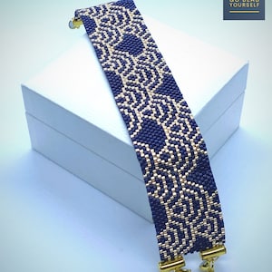 May include: A beaded bracelet with a geometric pattern in navy blue and gold. The bracelet is rectangular and has gold-colored clasps. The text "GO BEAD YOURSELF" is in the upper right corner.