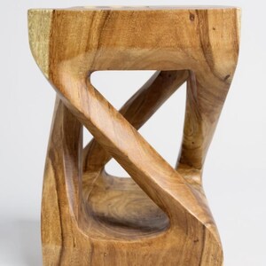 May include: A wooden stool with a unique, sculptural design. The stool is made of light brown wood and features an open, interwoven structure. The top and base are rectangular, and the sides have a twisted, geometric shape. The wood grain is visible.