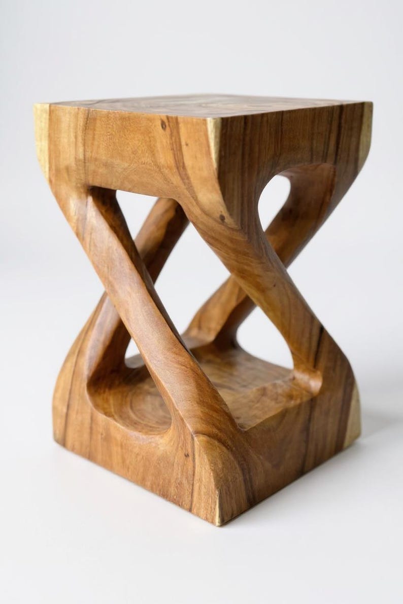 May include: A handcrafted wooden stool with a unique, intertwined design. The natural wood grain is visible, showcasing the warm brown tones of the material. The stool's dimensions are approximately 12 inches square and 18 inches tall.