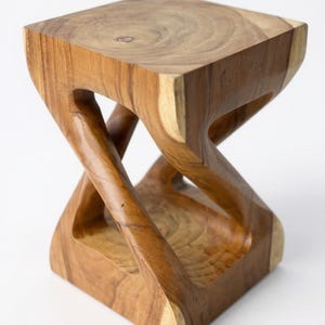 May include: A handcrafted wooden stool with a unique hourglass-like design. The square top and base are connected by intricately carved, curved supports. The natural wood grain and warm brown tones create a rustic, yet modern aesthetic.