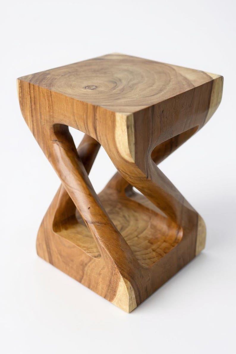 May include: A handcrafted wooden stool with a unique hourglass-like design. The square top and base are connected by intricately carved, curved supports. The natural wood grain and warm brown tones create a rustic, yet modern aesthetic.