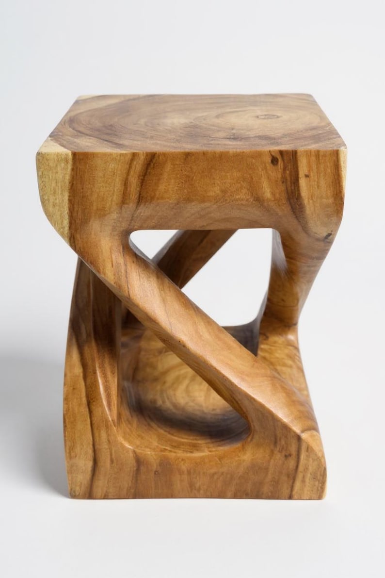 May include: A solid wood stool with a unique, sculptural design. The square seat rests on a base with a carved, openwork pattern. The natural wood grain and warm tones create a rustic, yet modern aesthetic. This piece is suitable for seating or as a decorative accent.