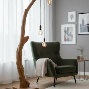 Könnte beinhalten: Eine einzigartige Stehlampe aus einem natürlichen Ast, mit drei hängenden Edison-Glühbirnen. Die Lampe steht auf einem Holzsockel, neben einem grünen Sessel und einer neutralfarbenen Decke. Der Raum hat eine moderne, minimalistische Ästhetik.