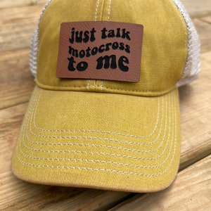 May include: A yellow and white baseball cap with a brown leather patch that says "just talk motocross to me".