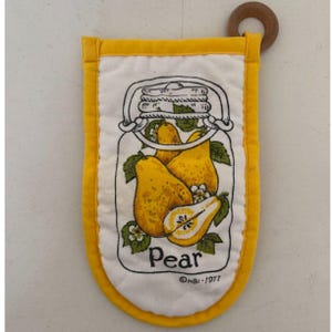 May include: A rectangular white quilted oven mitt with a bright yellow border and a wooden hanging ring. The center features a graphic of a mason jar filled with yellow pears, green leaves, and white blossoms, with the text "Pear" and "©HBI-1977".