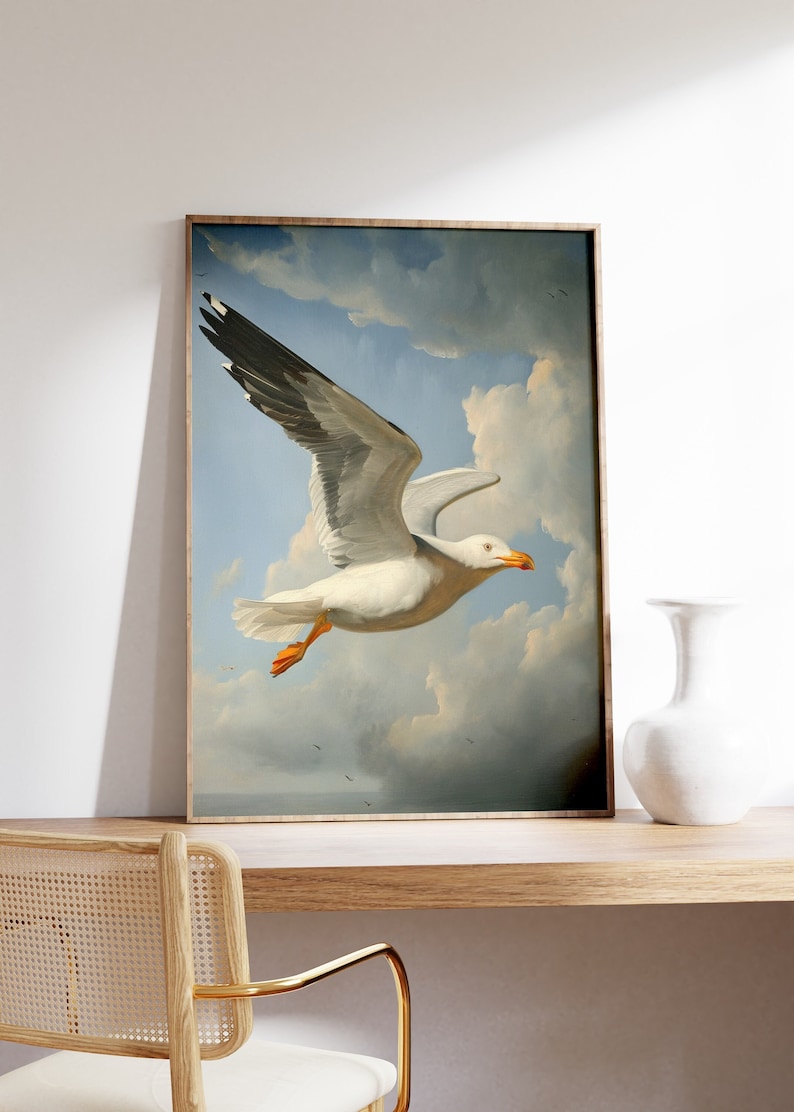 Puede incluir: Una pintura enmarcada de una gaviota blanca con puntas de alas negras volando contra un cielo azul con nubes blancas.
