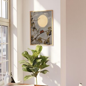May include: A framed art print with a botanical illustration. The artwork shows a full moon in a light blue sky, with a branch of berries and two ladybirds. The frame is a light wood colour.