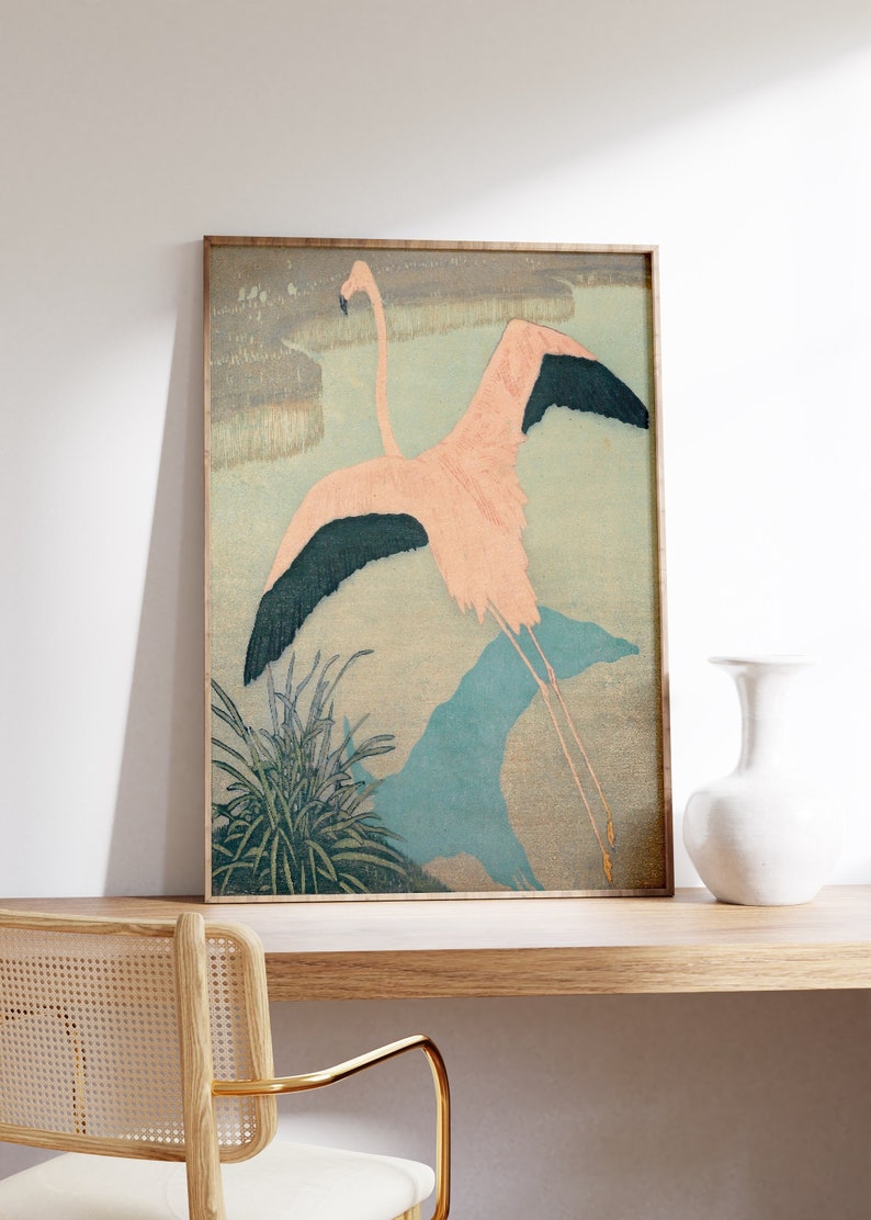 May include: A framed print of a pink flamingo with black wingtips flying over a blue and green landscape. The print is in a wooden frame.