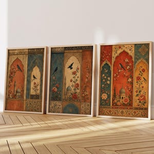 May include: Three framed art prints featuring a vintage design with arched windows, birds, and floral patterns. The color palette includes shades of orange, blue, and gold. The prints are displayed on a wooden floor against a white wall.