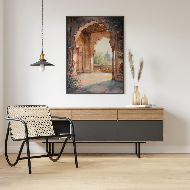 May include: A framed watercolor painting of an ornate archway with a view of a domed building in the distance. The archway is decorated with intricate carvings and floral details. The painting is set against a white wall with a black pendant light hanging above it.