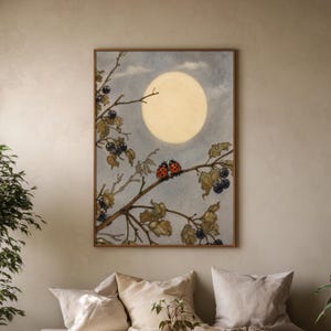 May include: A framed watercolour print depicting a full moon in a cloudy sky. Two ladybirds sit on a branch with leaves and berries. The artwork has a vintage, whimsical feel.