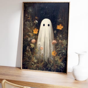 K&ouml;nnte beinhalten: Gerahmter Kunstdruck mit einem wei&szlig;en Geisterwesen mit schwarzen Augen, das inmitten eines Gartens mit orangefarbenen und rosa Blumen steht. Das Kunstwerk hat eine Vintage-&Auml;sthetik, mit dunklem Hintergrund und Holzrahmen. Der Druck wird auf einer Holzoberfl&auml;che pr&auml;sentiert.