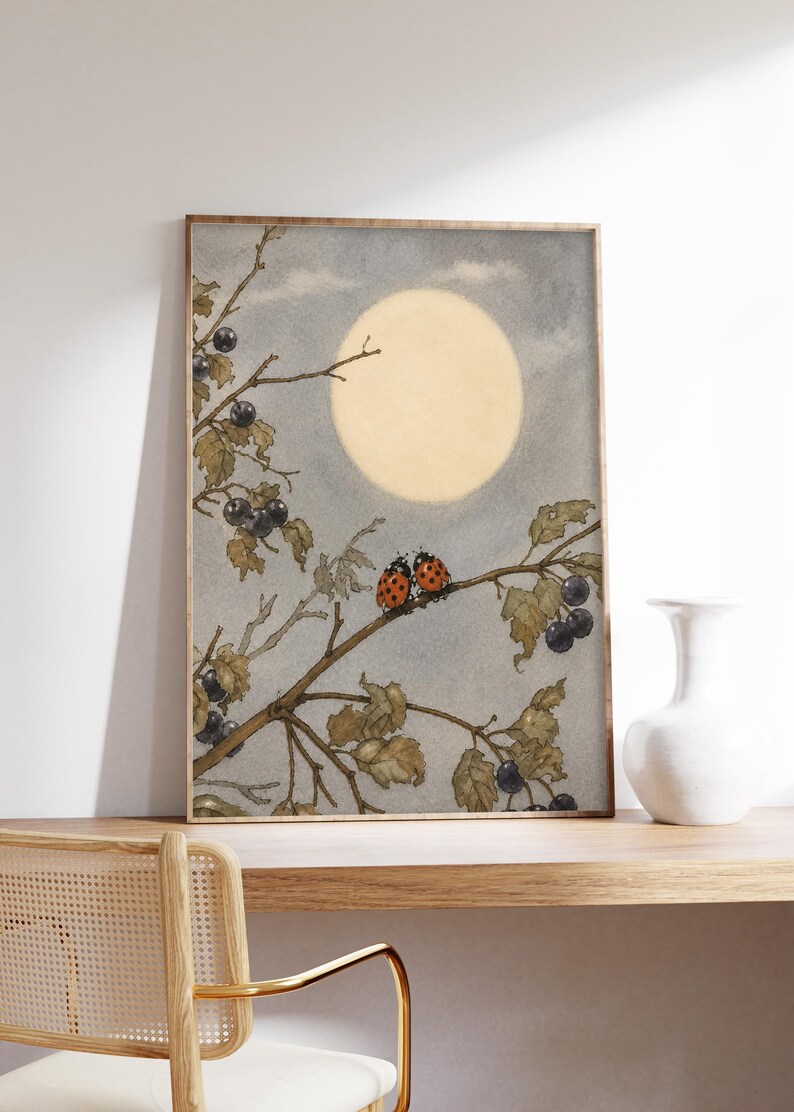 May include: A framed watercolour print depicting a tranquil scene with a large, pale yellow moon in a grey sky. Two ladybirds sit on a branch with leaves and dark berries. The artwork has a vintage aesthetic.