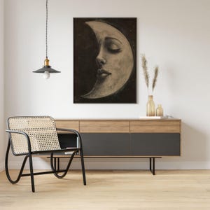 Op de afbeelding: Een zwart-witte illustratie van een wassende maan met een vrouwen gezicht. De maan is afgebeeld met gesloten ogen en een zachte uitdrukking. De achtergrond is donkergrijs met een paar witte sterren.