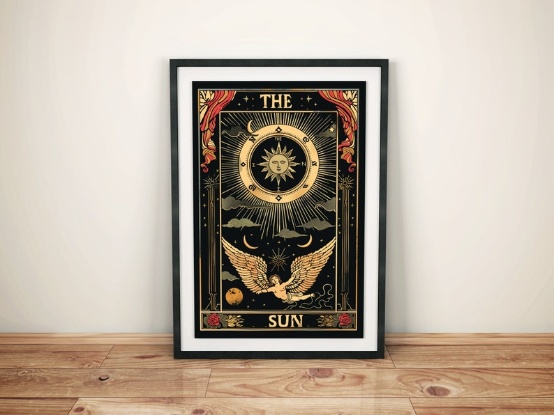 Op de afbeelding: Een zwarte en gouden tarotkaart met het woord "THE SUN" onderaan. De kaart toont een zon met een gezicht, een engel met vleugels en een wassende maan.