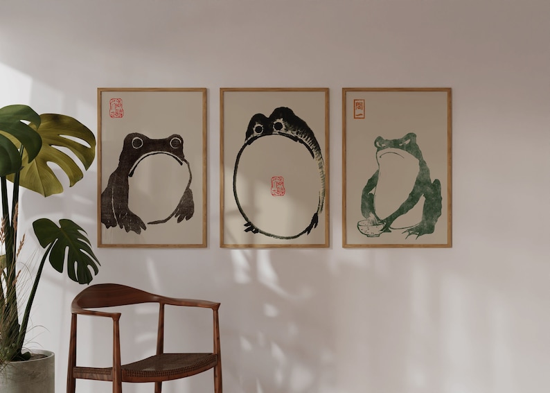 May include: Three framed prints of black and green frogs on a white wall. The frogs are in different poses, one is curled up in a circle, one is sitting with its legs crossed, and one is sitting with its legs straight out.