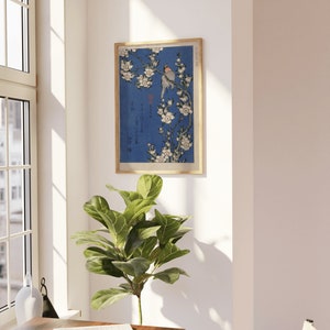 May include: A framed print of a Japanese woodblock print depicting a bird perched on a branch of white cherry blossoms against a blue background. The print is in a wooden frame.