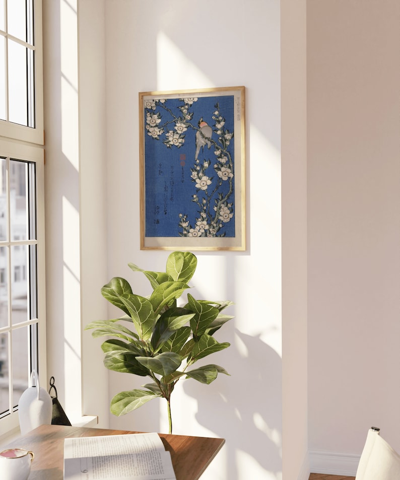 May include: A framed print of a Japanese woodblock print depicting a bird perched on a branch of white cherry blossoms against a blue background. The print is in a wooden frame.