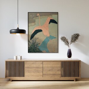 May include: A framed print of a pink flamingo in flight against a blue and green background. The print is hanging on a white wall above a wooden cabinet with two doors.