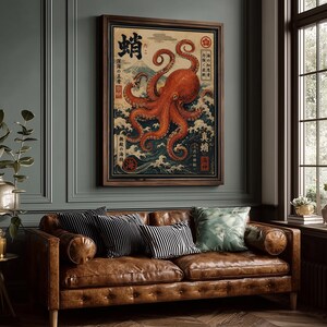 May include: A framed wall art print featuring a large orange octopus centered over stylized blue ocean waves and a mountain peak in the background. The artwork includes Japanese kanji characters and red circular stamps on a cream-colored paper background.