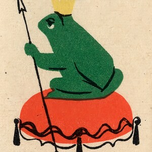 Op de afbeelding: Een groene kikker met een gouden kroon zit op een rood kussen met een zwart-witte rand. De kikker houdt een speer vast met een pijlpunt. De tekst "Царевна-лягушка" staat bovenaan de afbeelding in het zwart.