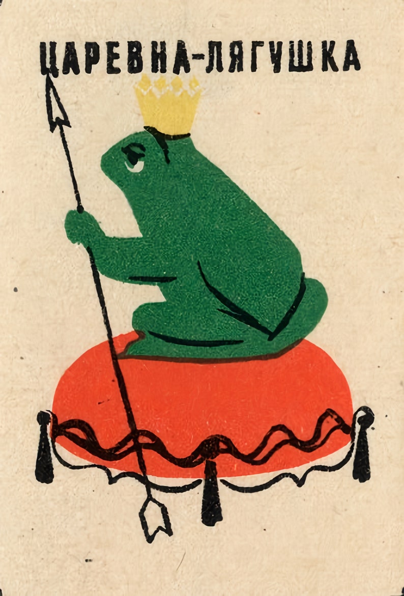 Op de afbeelding: Een groene kikker met een gouden kroon zit op een rood kussen met een zwart-witte rand. De kikker houdt een speer vast met een pijlpunt. De tekst "Царевна-лягушка" staat bovenaan de afbeelding in het zwart.