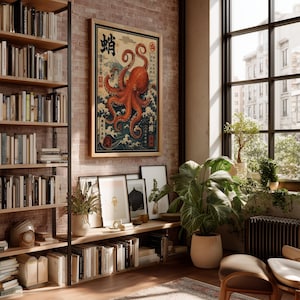 May include: A framed wall art print featuring a large orange octopus over stylized blue ocean waves with Mount Fuji in the background and Japanese text characters, displayed on a brick wall in a room with bookshelves and a large window.