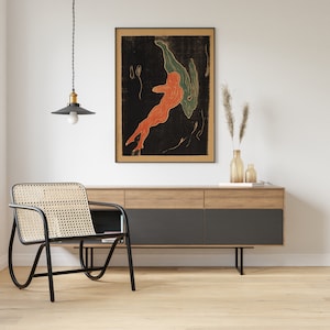 May include: A black framed print of a red and green abstract figure on a black background hangs above a wooden dresser with black drawers. A black wicker chair sits in front of the dresser.