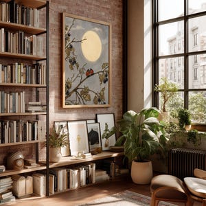 May include: An interior scene with a brick wall, a large window, and a wooden bookshelf filled with books. A framed artwork depicts a moonlit scene with branches and berries. Potted plants and a rug add warmth to the room. A comfortable chair is in the foreground.