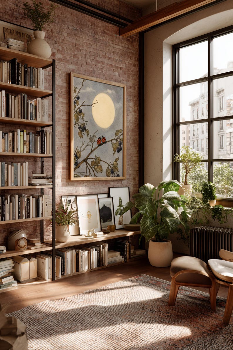 May include: An interior scene with a brick wall, a large window, and a wooden bookshelf filled with books. A framed artwork depicts a moonlit scene with branches and berries. Potted plants and a rug add warmth to the room. A comfortable chair is in the foreground.