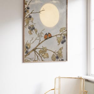 May include: A framed art print with a watercolour illustration of a moonlit scene. Two ladybirds sit on a branch with berries, set against a soft blue sky and a large, glowing moon. The artwork has a vintage aesthetic.